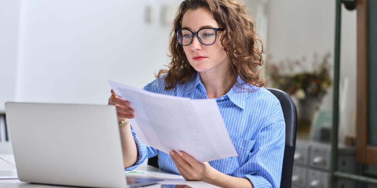 Lady holding sheets of paper in front of her laptop