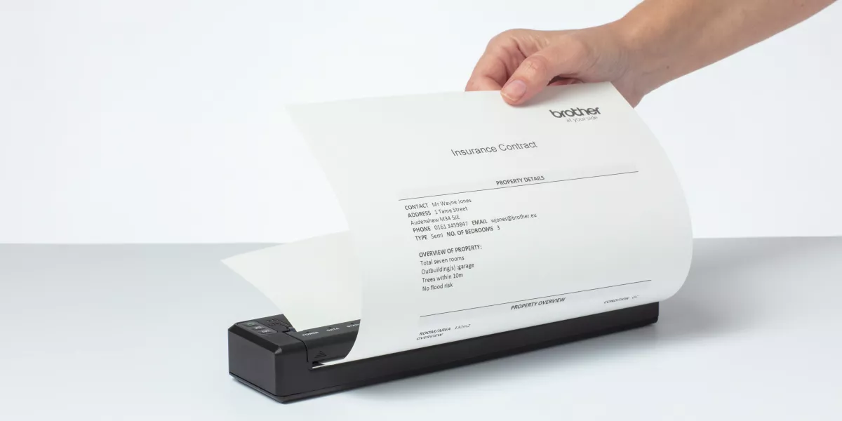 A hand printing a sheet of paper from a Brother A4 portable printer