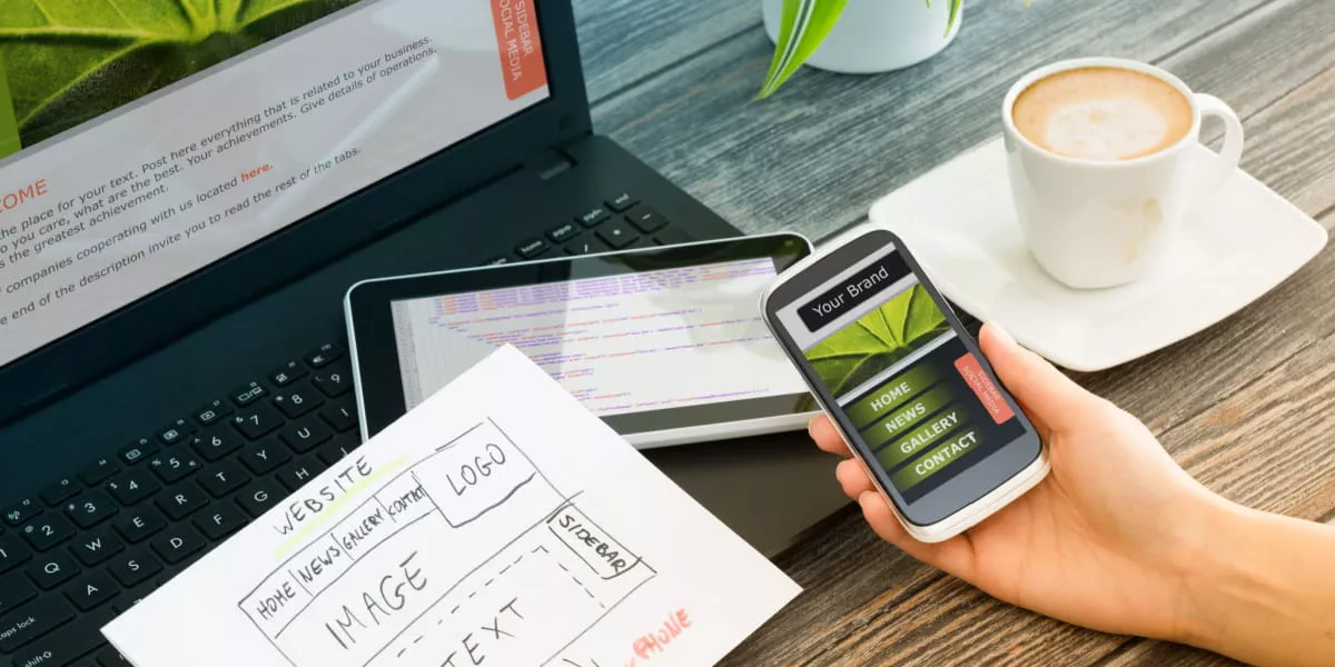 A person's hand with a smartphone working on brand design on laptop