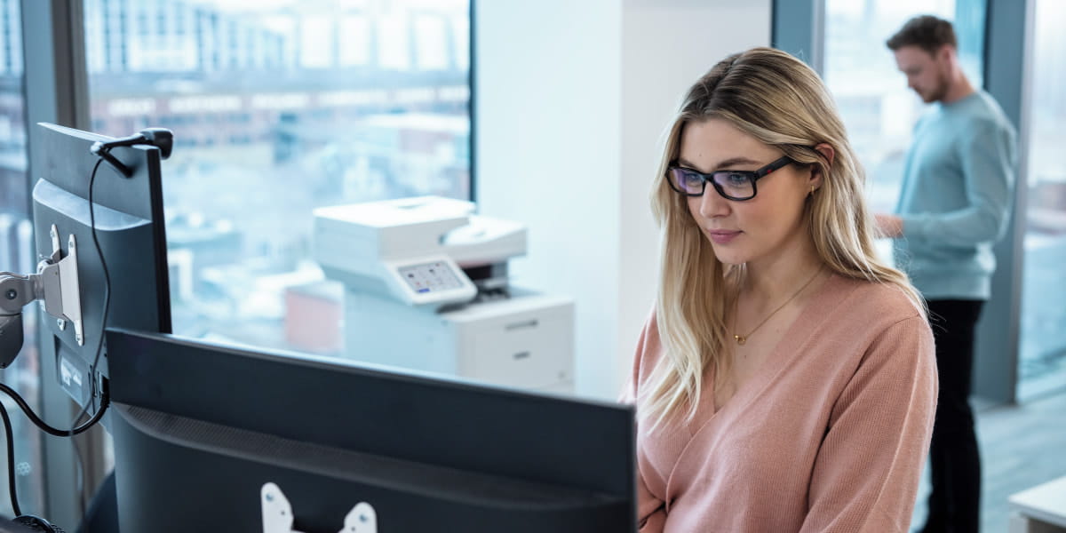 Two colleagues working near a multi-function printer in an office