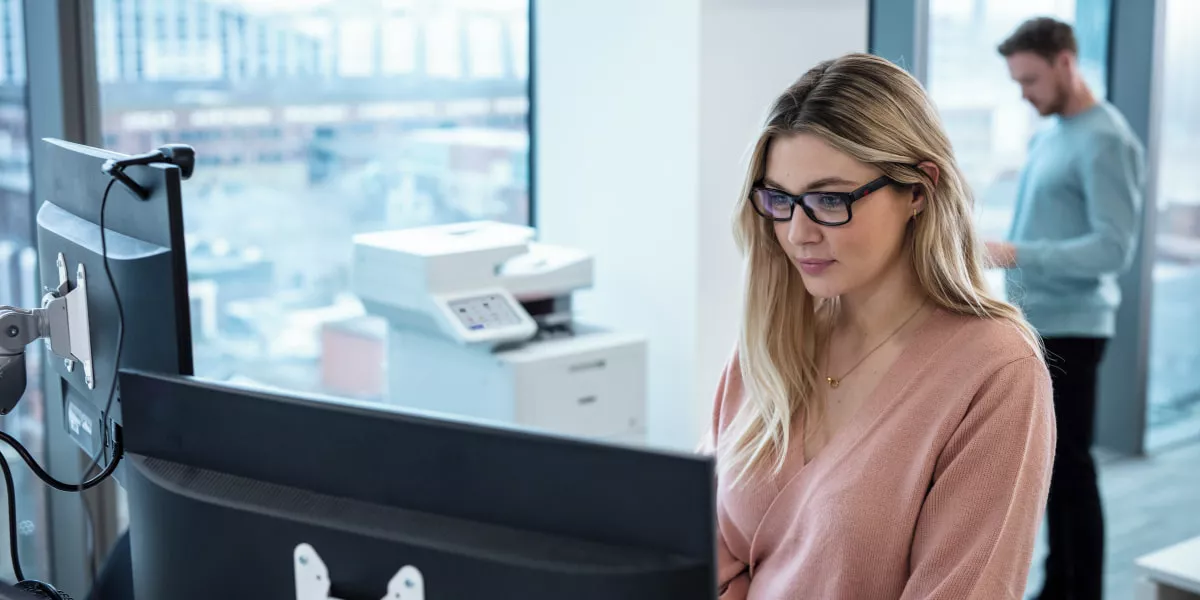 Two colleagues working near a multi-function printer in an office