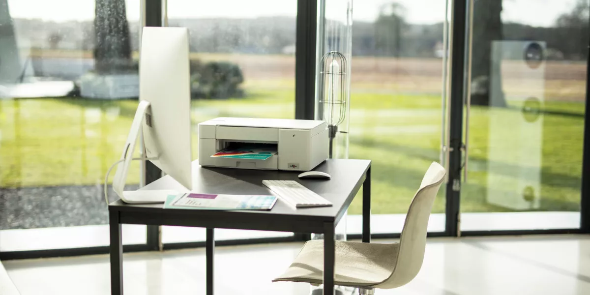 A workstation overlooking nature with a Brother DCP-J1200 XL printer and computer