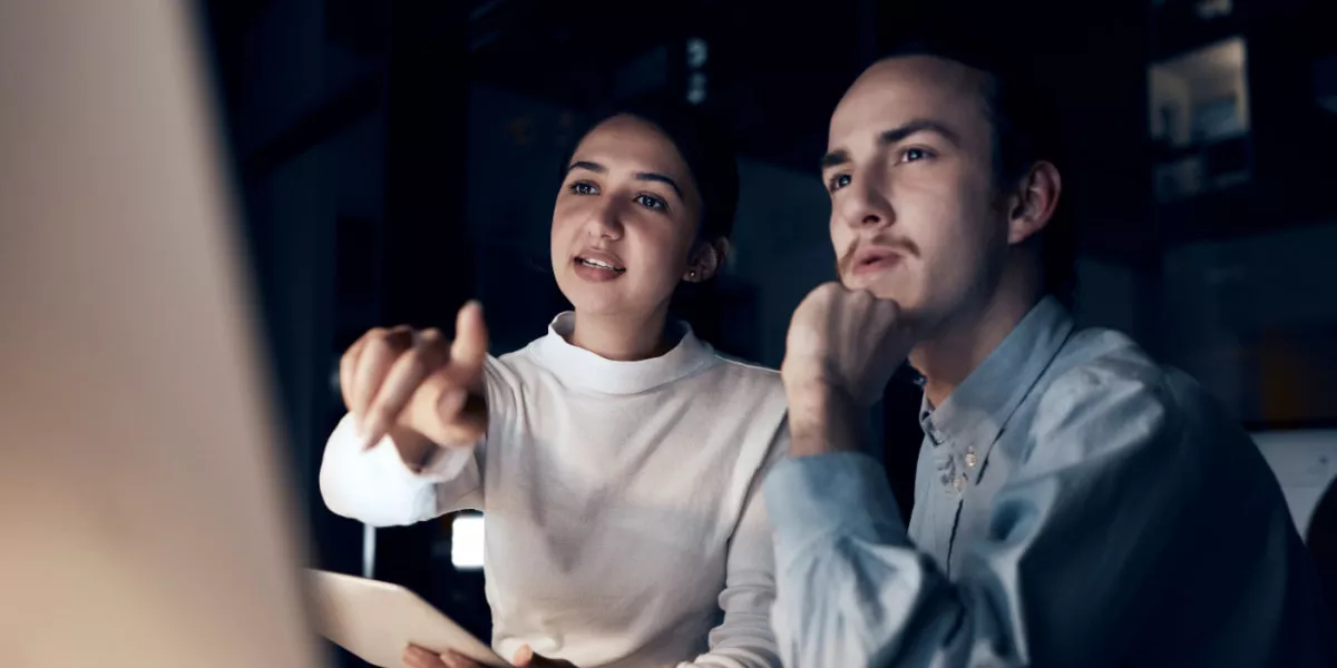 Two young professionals in front of a computer screen in a dark room