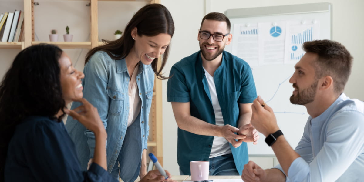 Four employees laughing and sharing conversation in an office meeting room