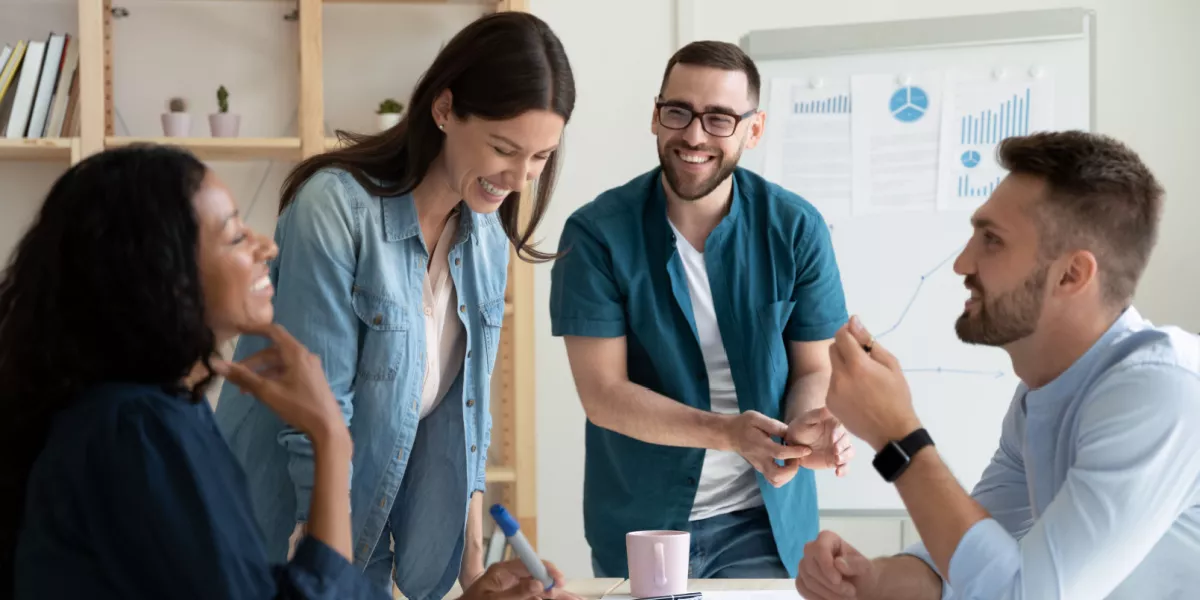 Four employees laughing and sharing conversation in an office meeting room