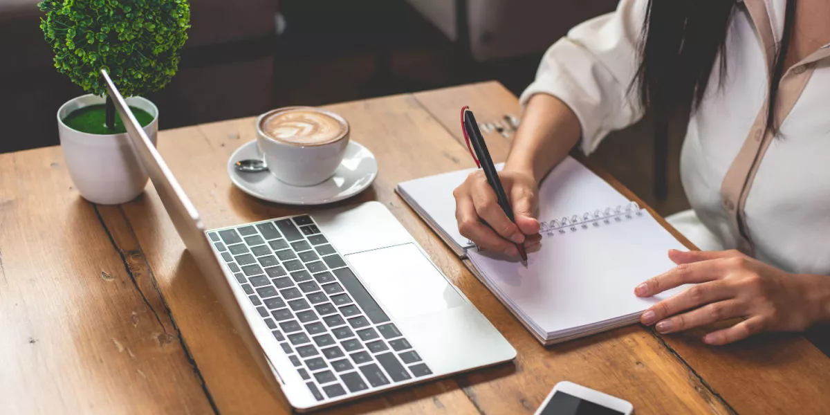 Lady writing down sustainable goals in front of laptop.