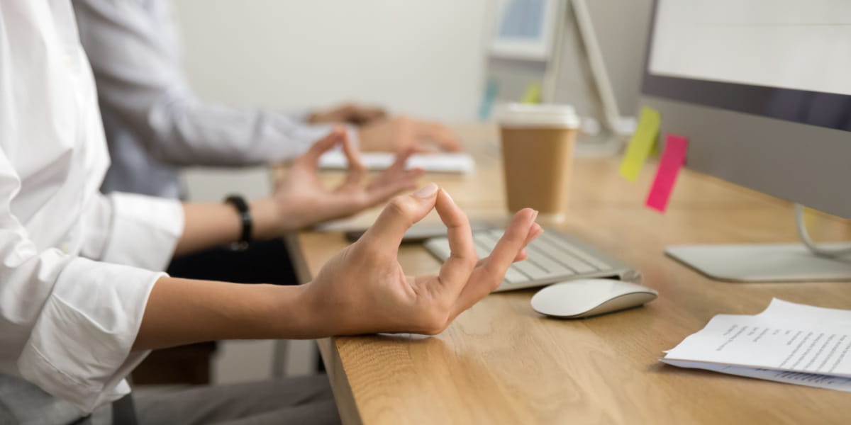 Person's hands meditating at work desk in front of a screen