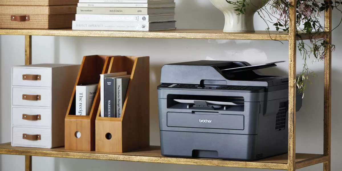 A monochrome laser printer in a home office bookshelf 