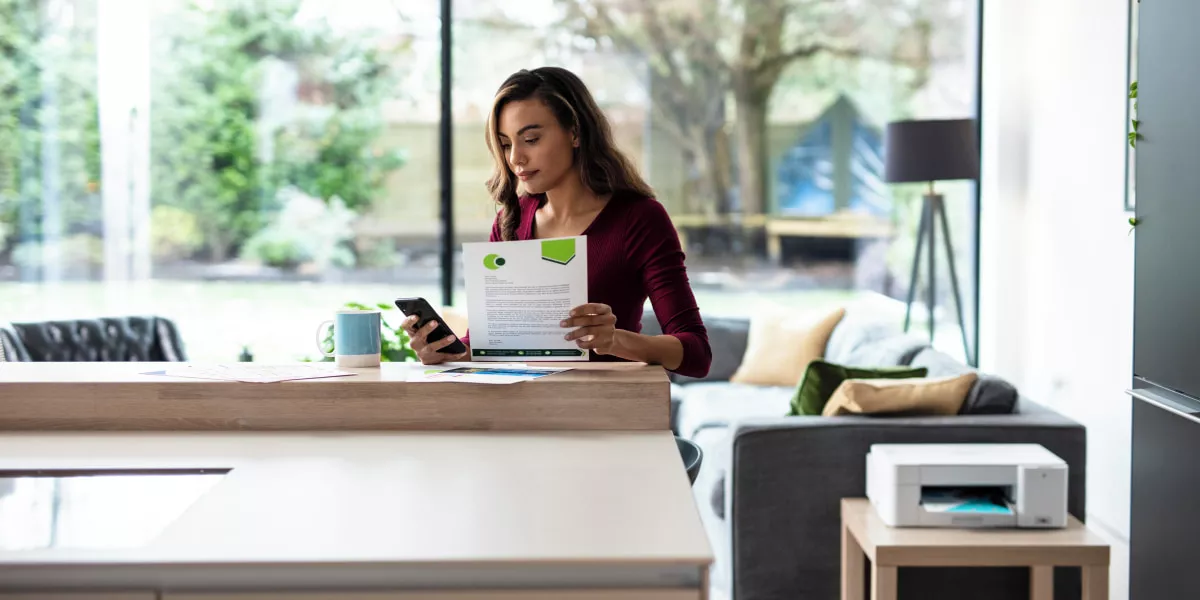 A lady working from home looking at a document next to a Brother INKvestment printer