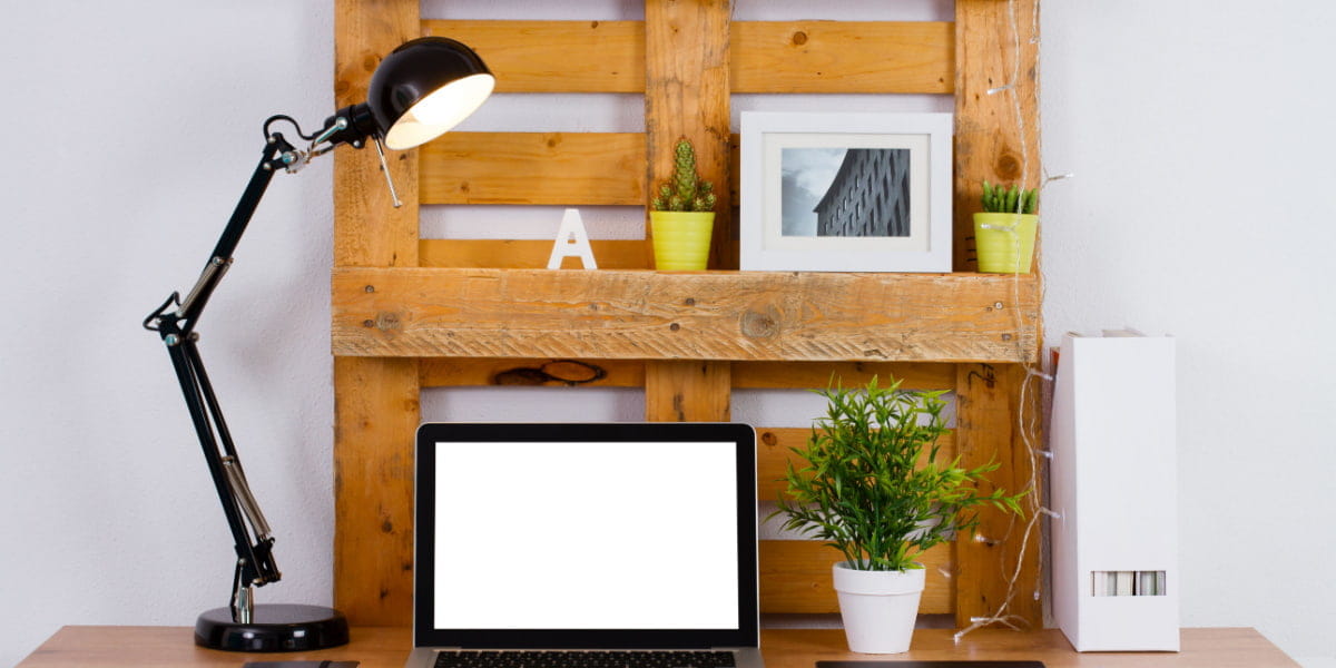A wooden pallet that's been upcycled as a home office desk with a lamp and laptop