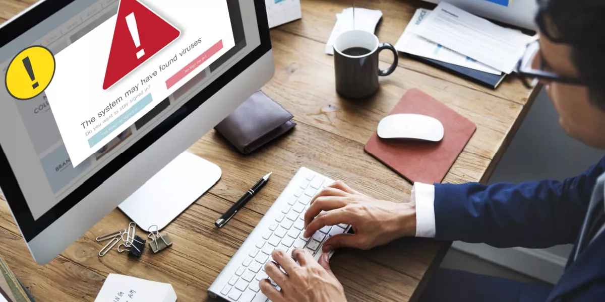 A man on a computer with a virus warning symbol on screen