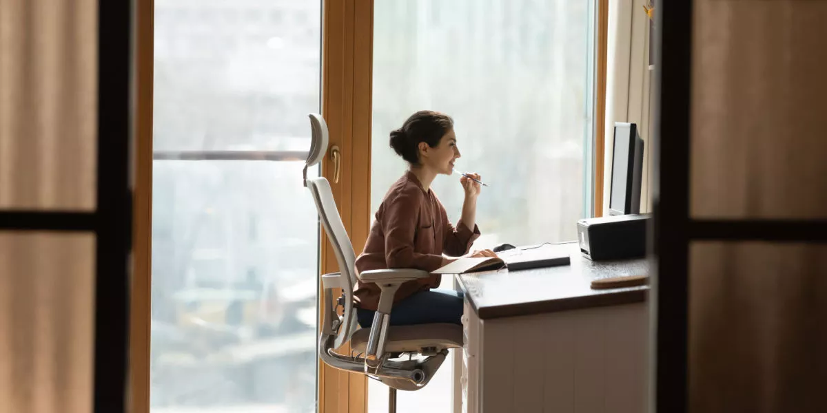A lady sitting in an ergonomic chair and desk in front of a computer.