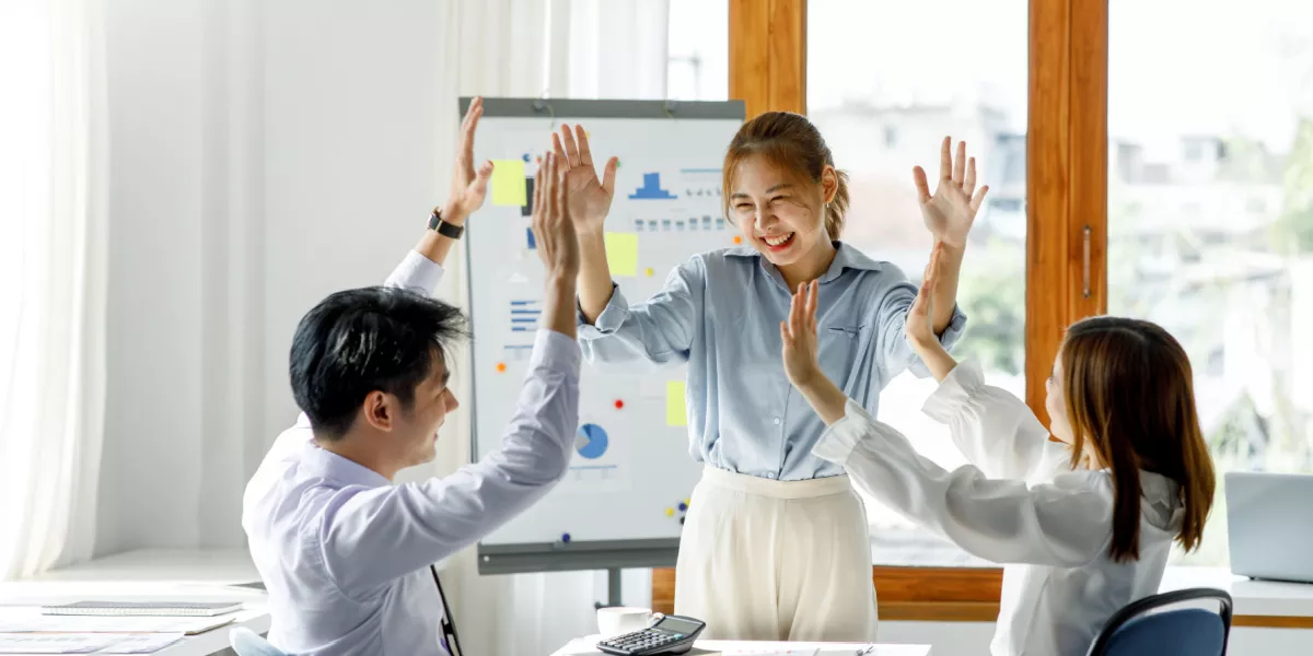 Three colleagues happily sharing success in a boardroom in front of a whiteboard