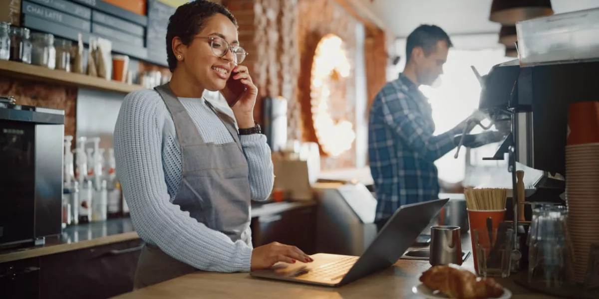 A cafe owner on the phone with a co-worker making coffee next to her