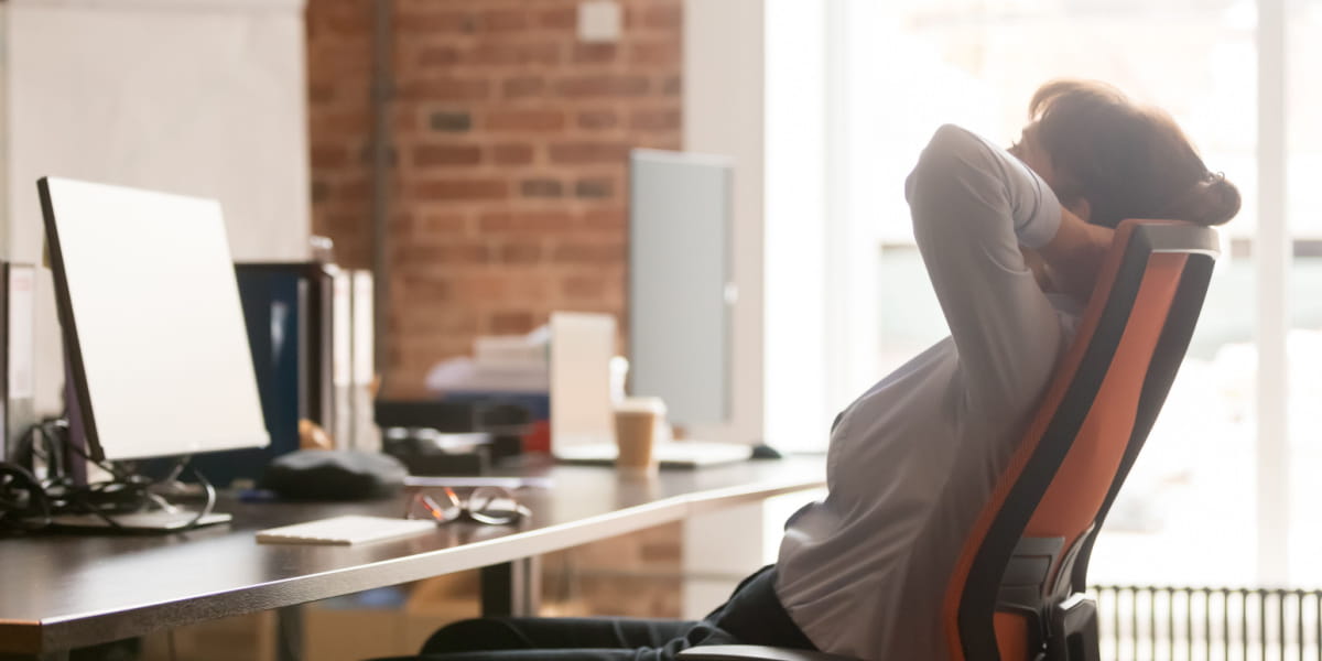 Person stretching in chair at home office in front of a computer