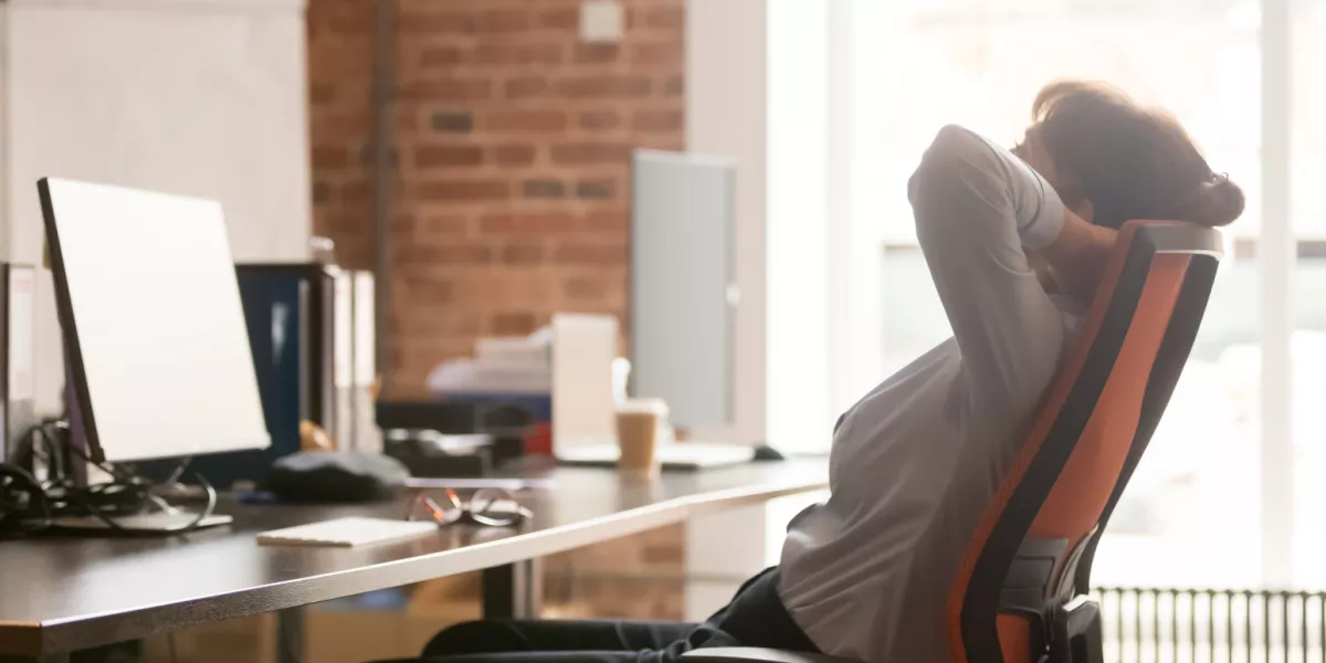 Person stretching in chair at home office in front of a computer