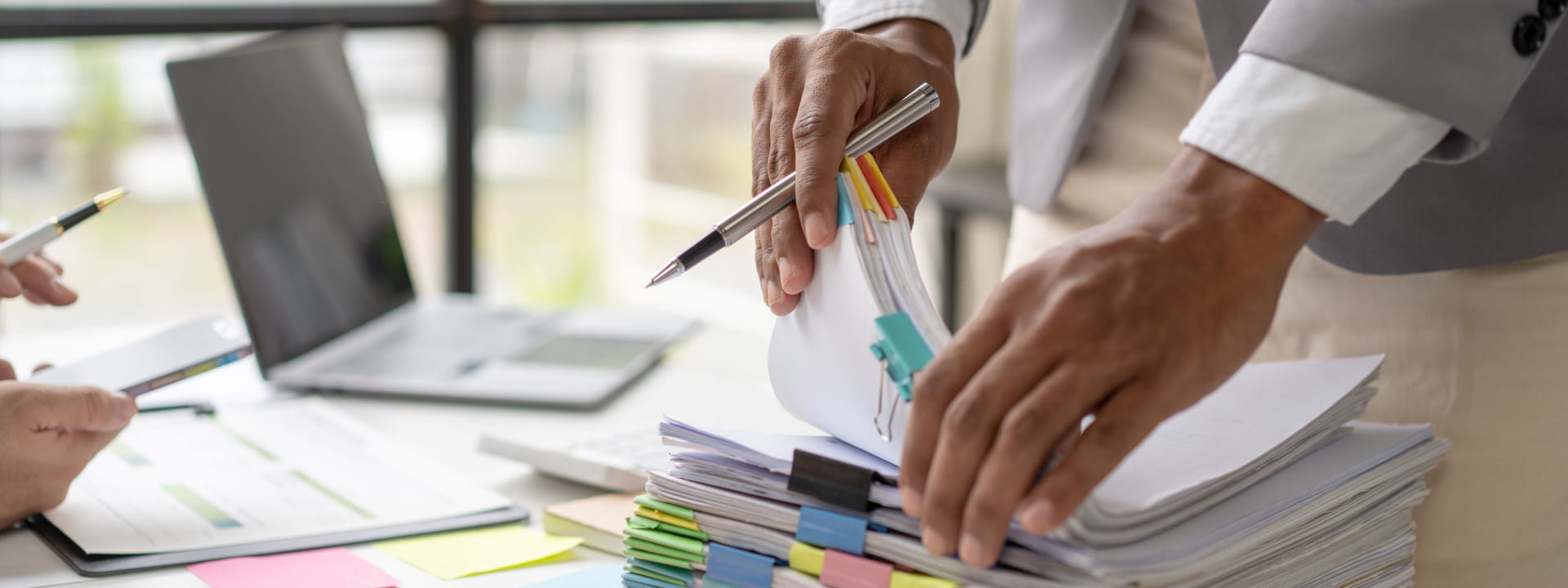 A businesswoman sorting through printed documents next to a laptop in an office environment