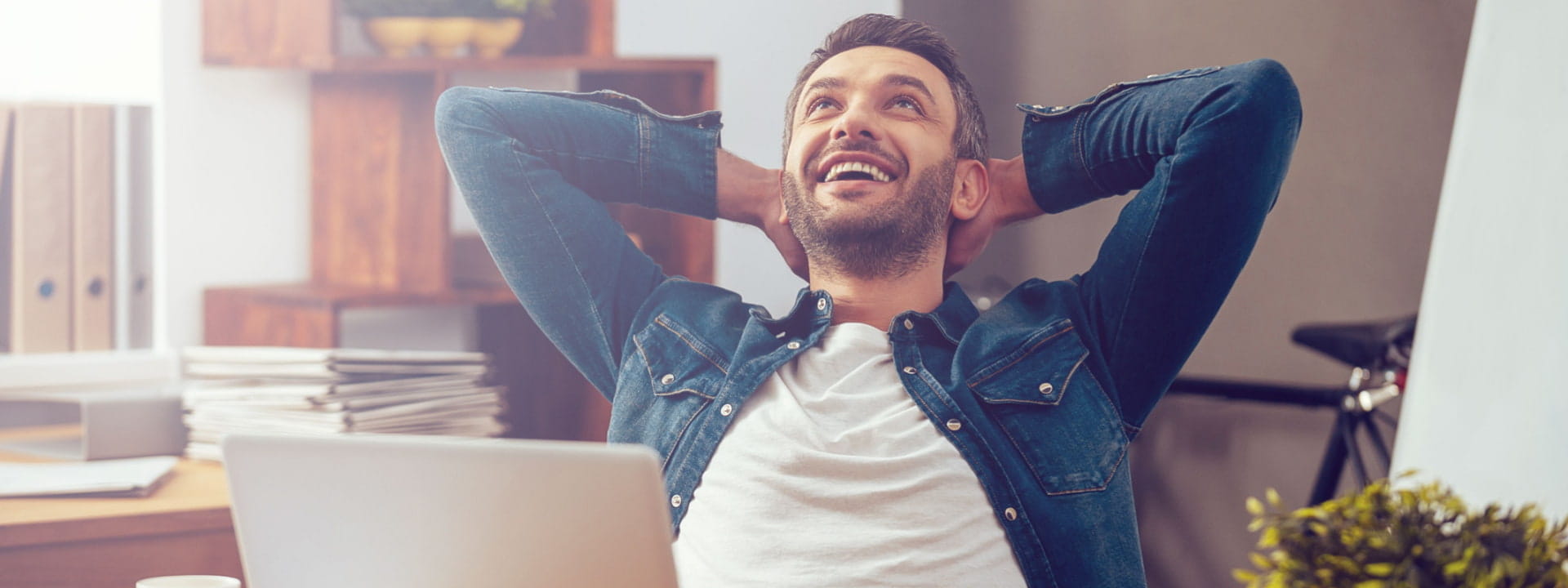 Man stretching happily at his work desk in front of a laptop