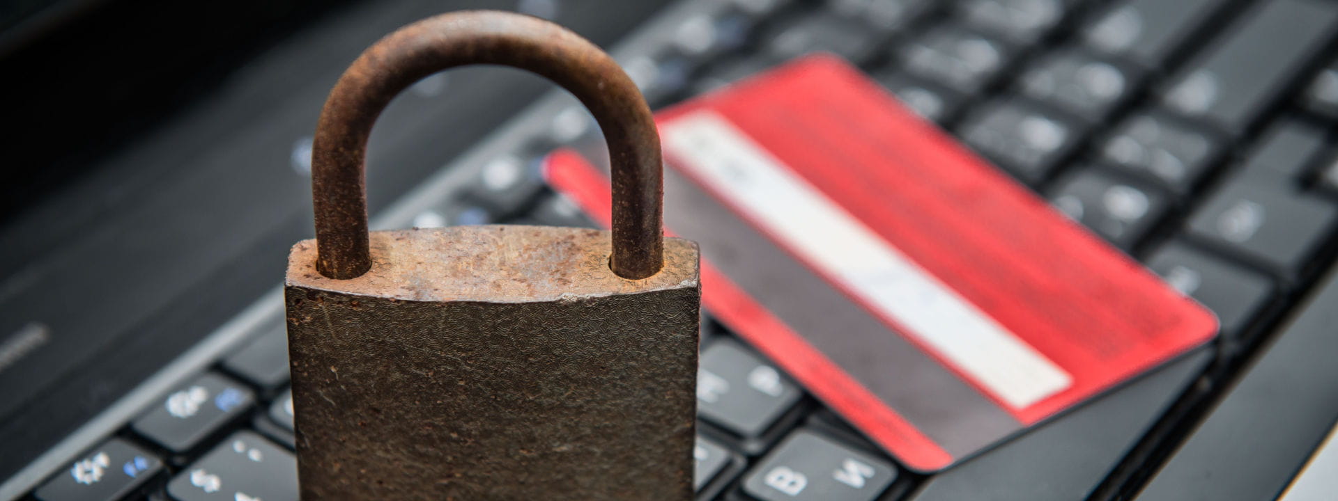 A rusty padlock and red credit card on a keyboard depicting ecommerce fraud.
