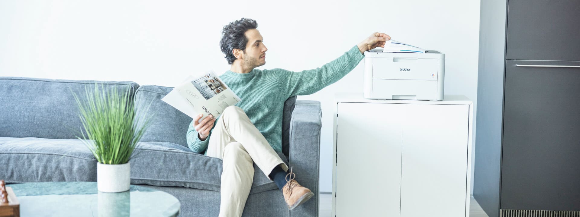 Man printing a document at home on a lounge from a colour laser printer