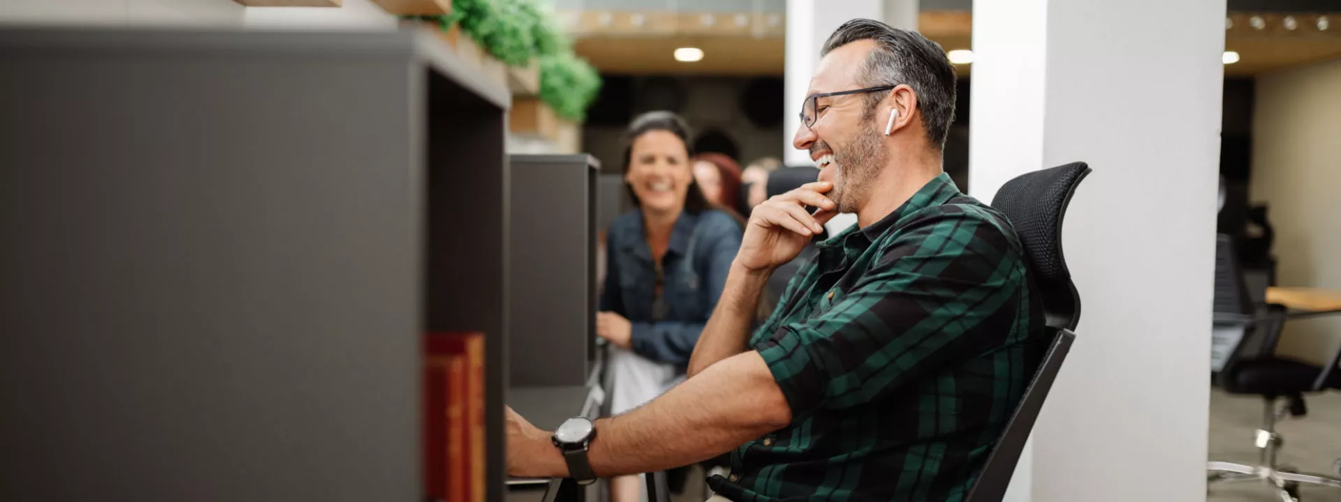 Man hot desking in office environment with co-worker talking