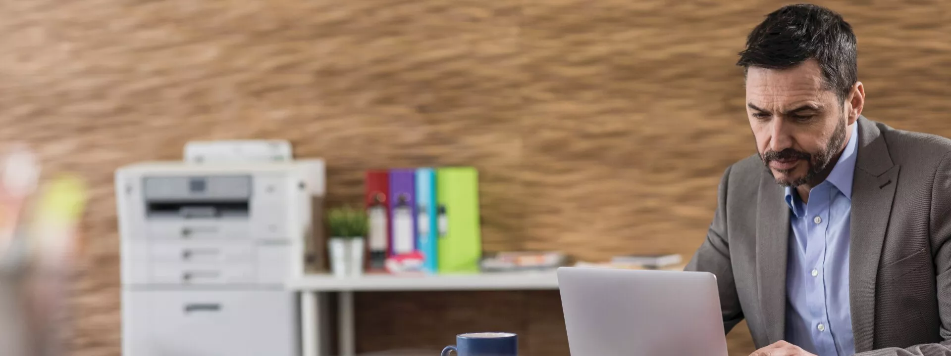 Man on his laptop with a Brother inkjet printer and workstation in the background.