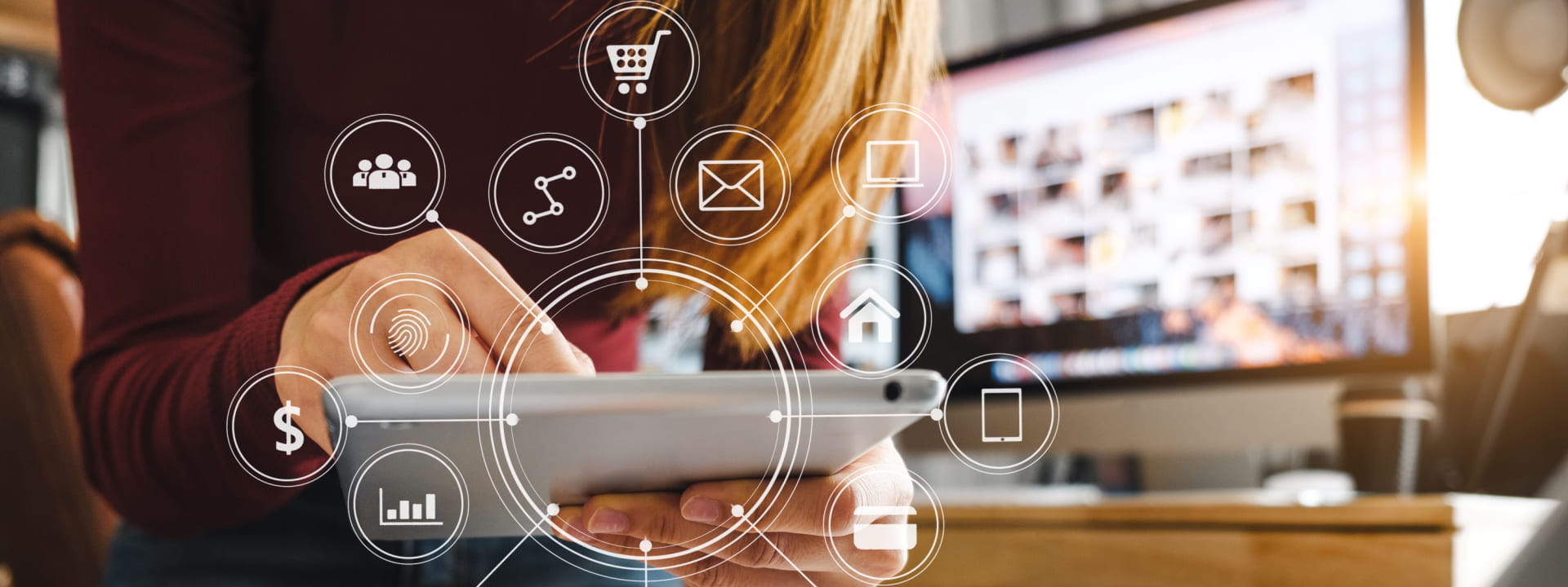 Lady using a tablet with multiple digital marketing icons next to a computer screen