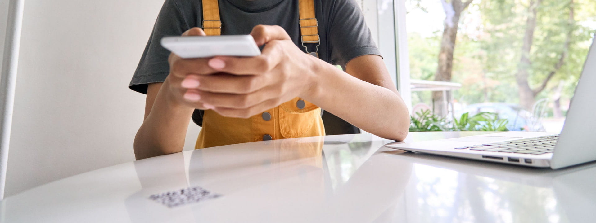 Lady on smartphone scanning a QR code at home next to a laptop