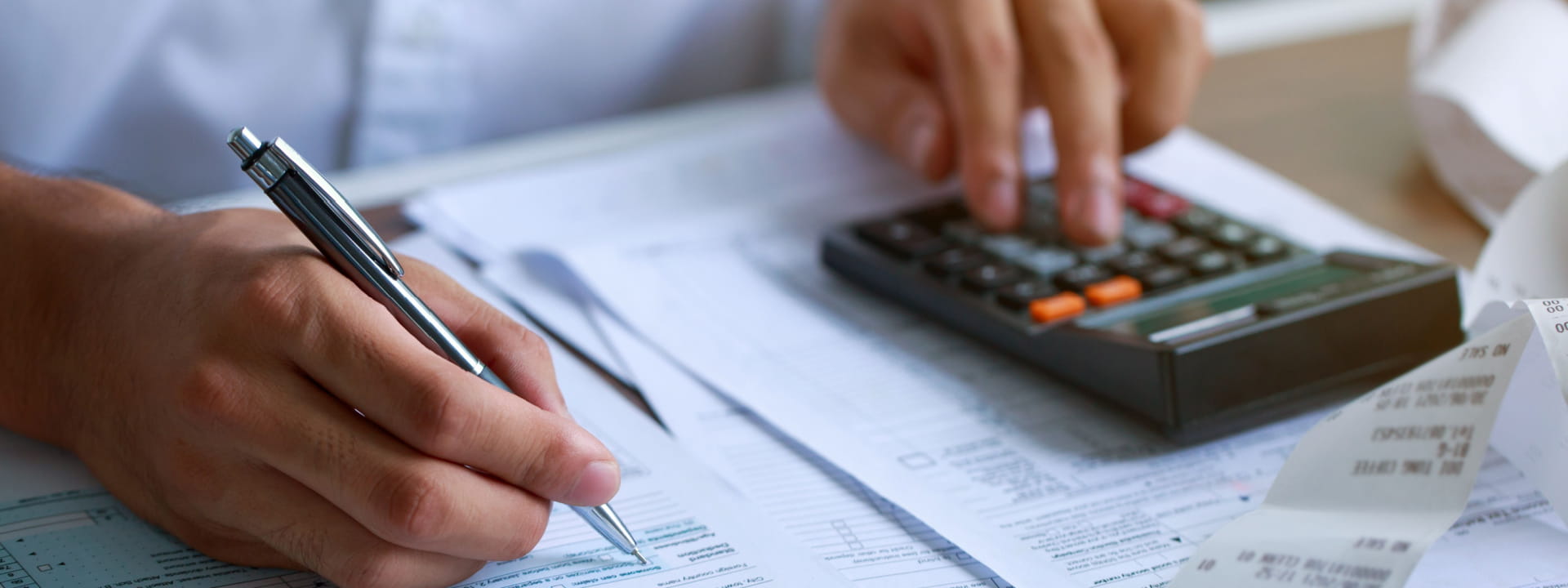 Hands with a pen and calculator working out taxes on paper