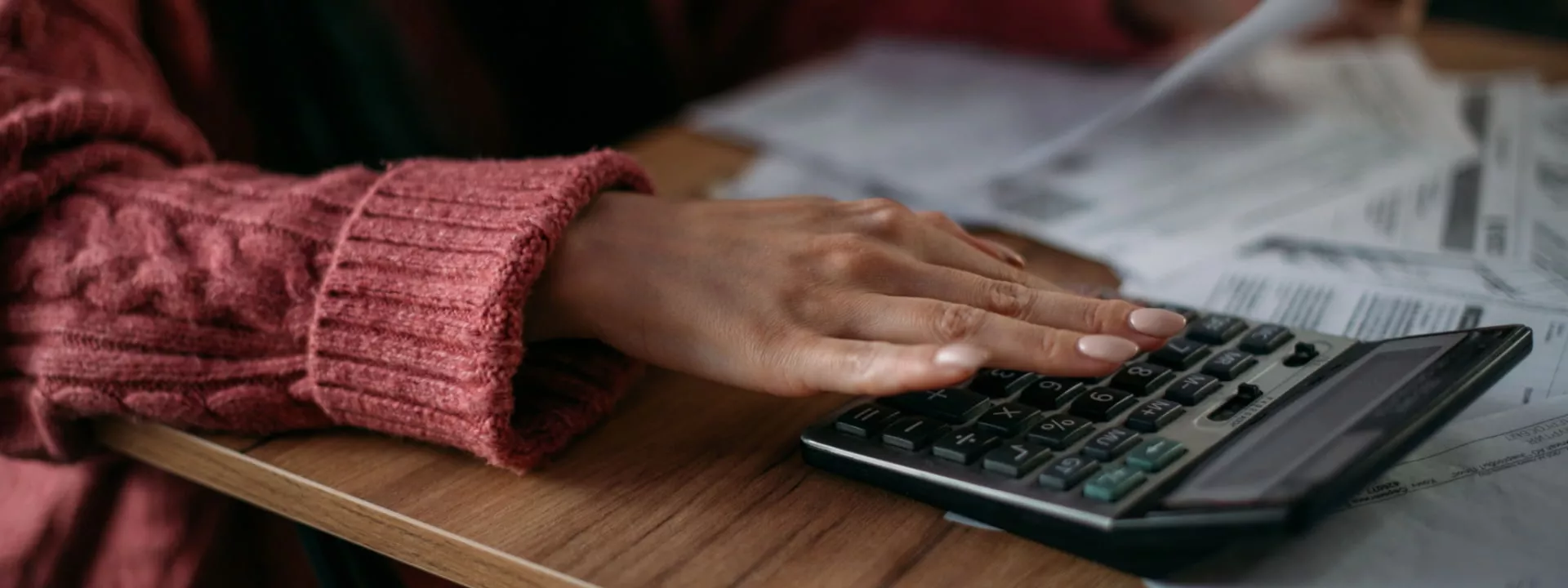 A lady's hand calculating bills with a calculator depicting rising cost of living