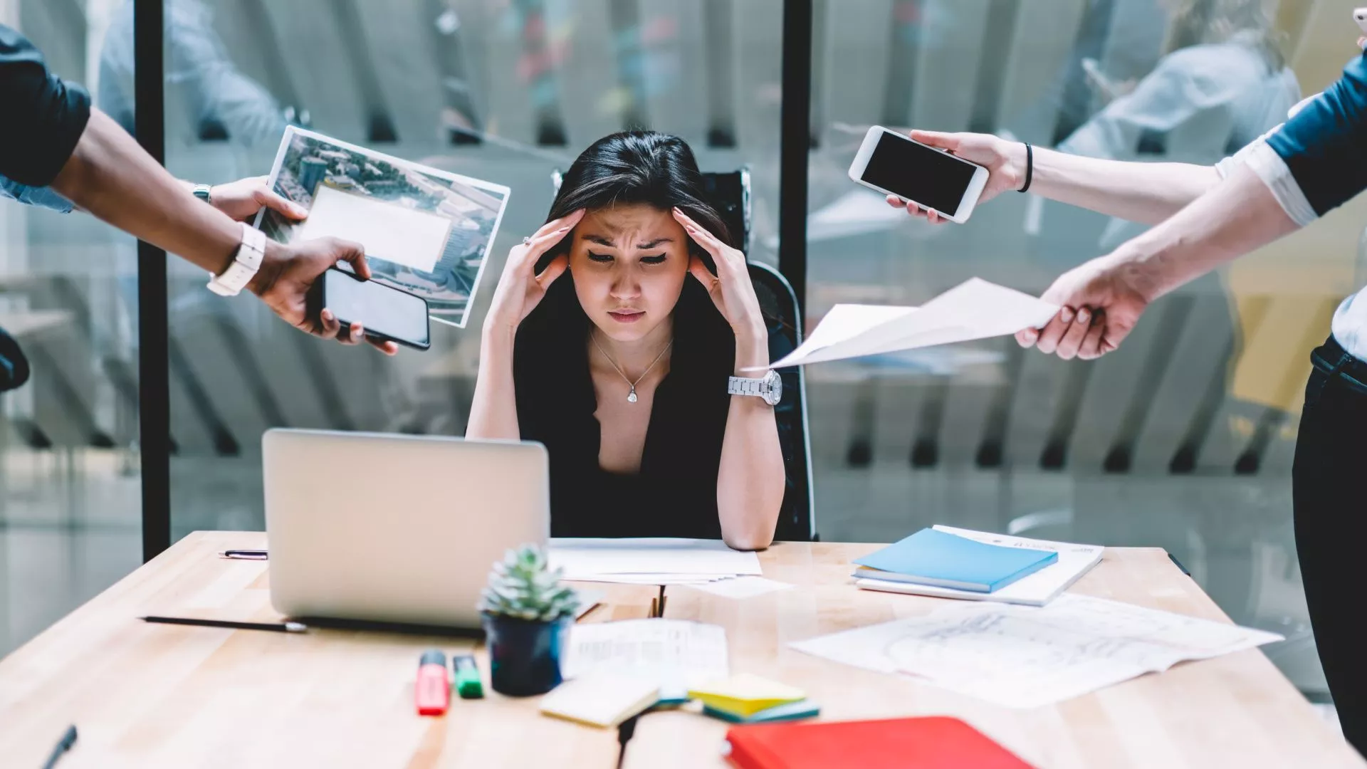 A lady with her hands on her head stressed with multiple hands giving her documents and items.