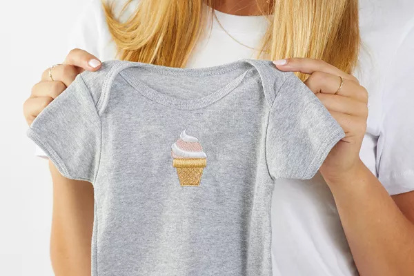 image of a person holding up a baby onesie with a machine embroidered design