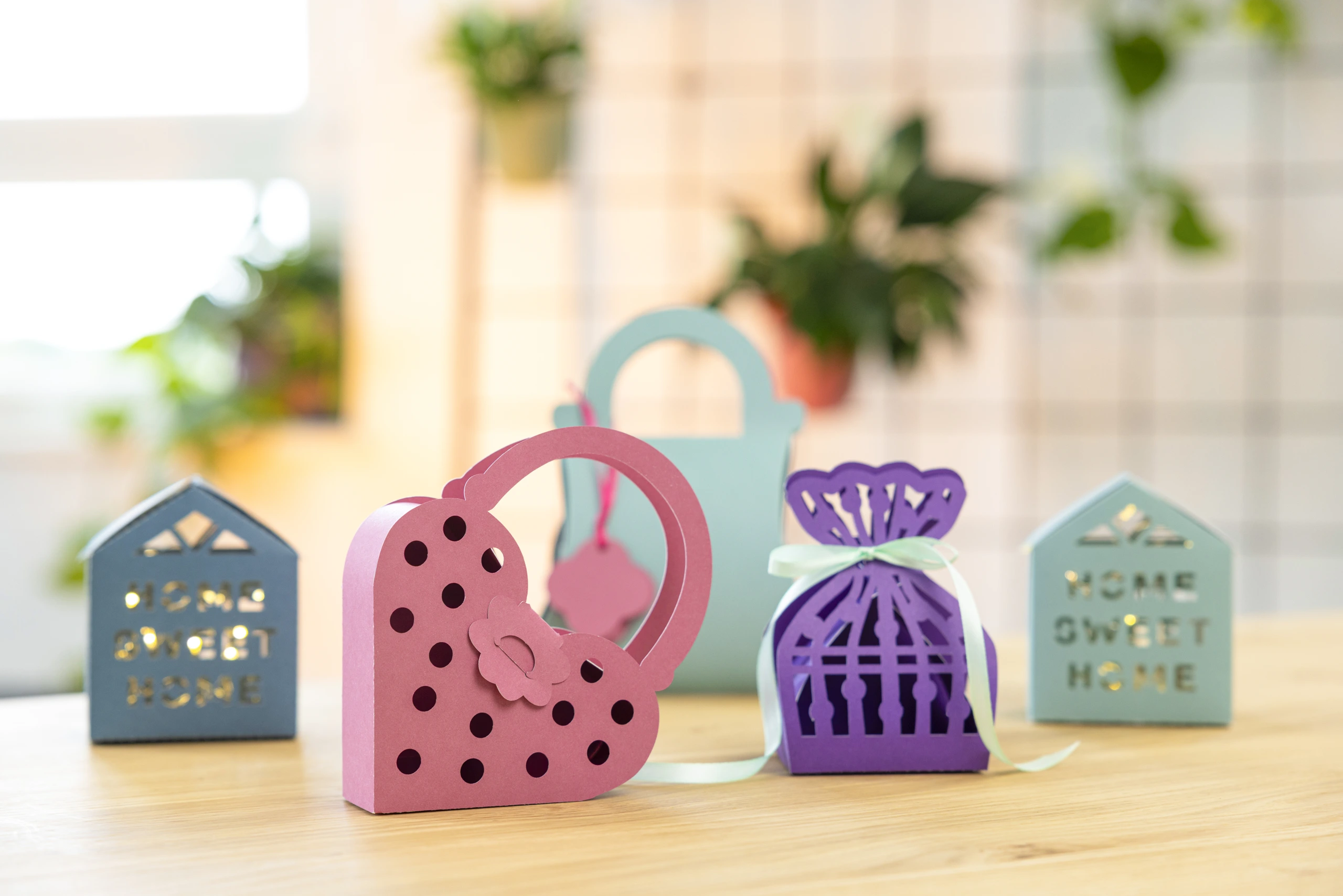Colourful paper craft gift bags and decorative house lanterns arranged on a wooden table.