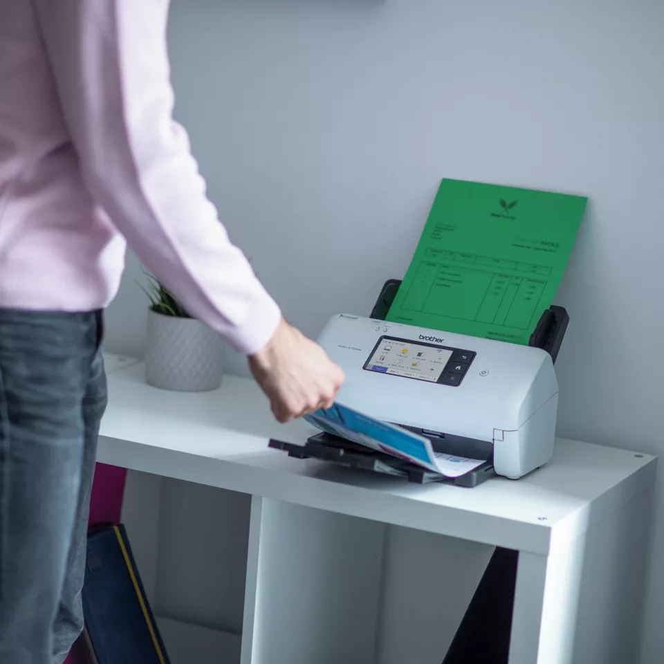 ADS-4700W sitting on a desk with a person removing the paper from the tray