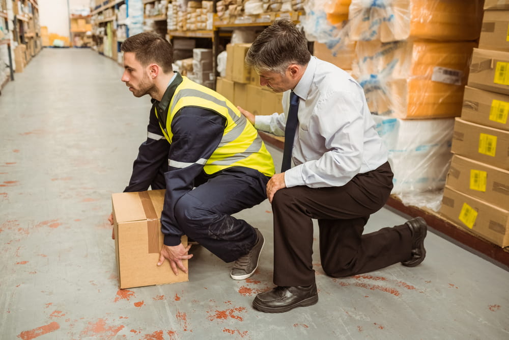 A warehouse worker receiving training on how to pick up a product carton safely.