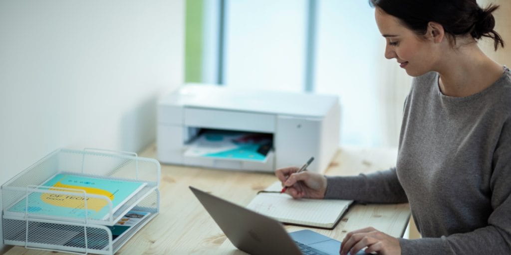 A lady jotting down notes next to a laptop and INKvestment printer.
