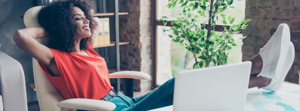 A young lady working from a home office with her feet up in front of her laptop.