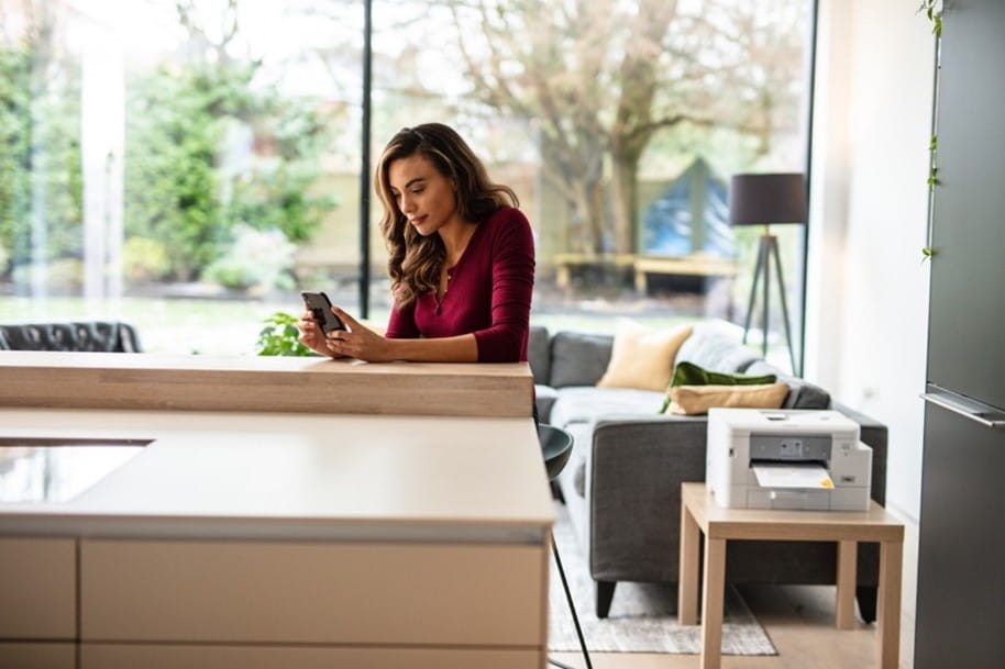 Young lady working from home on her smartphone next to a printer