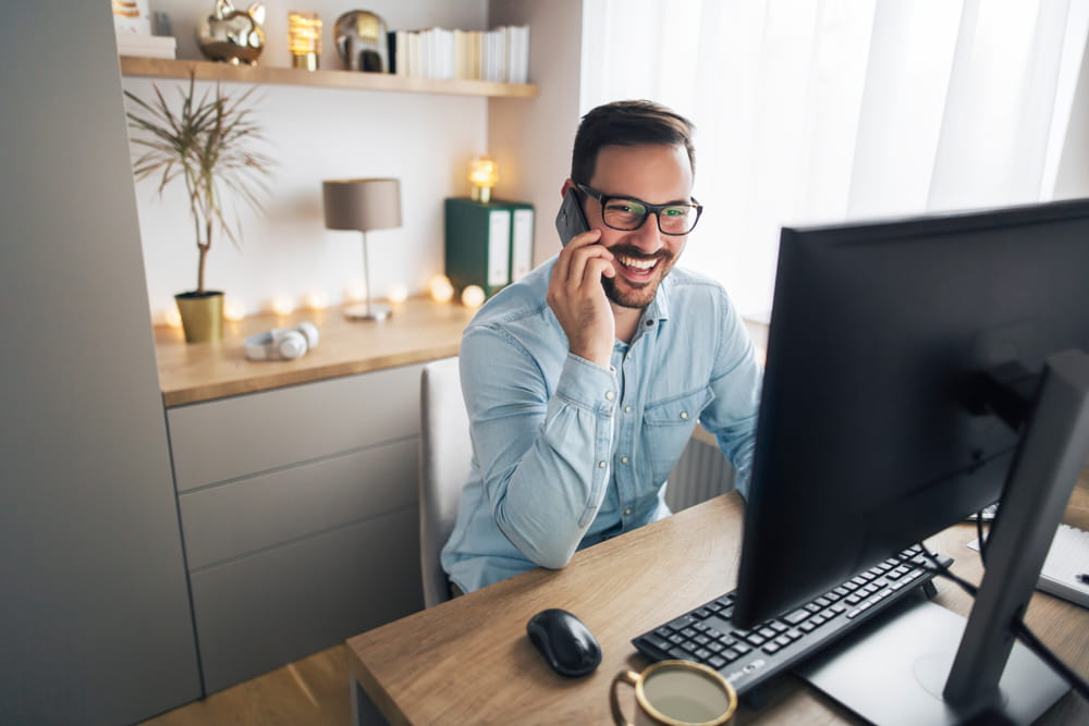 Young man smiling on phone in front of computer